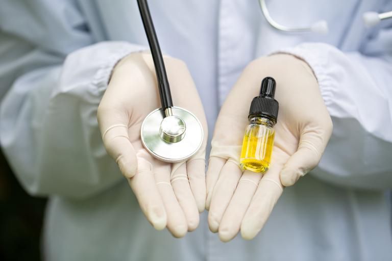 A Dr.'s hands holding a stethoscope and a bottle of CBD oil.